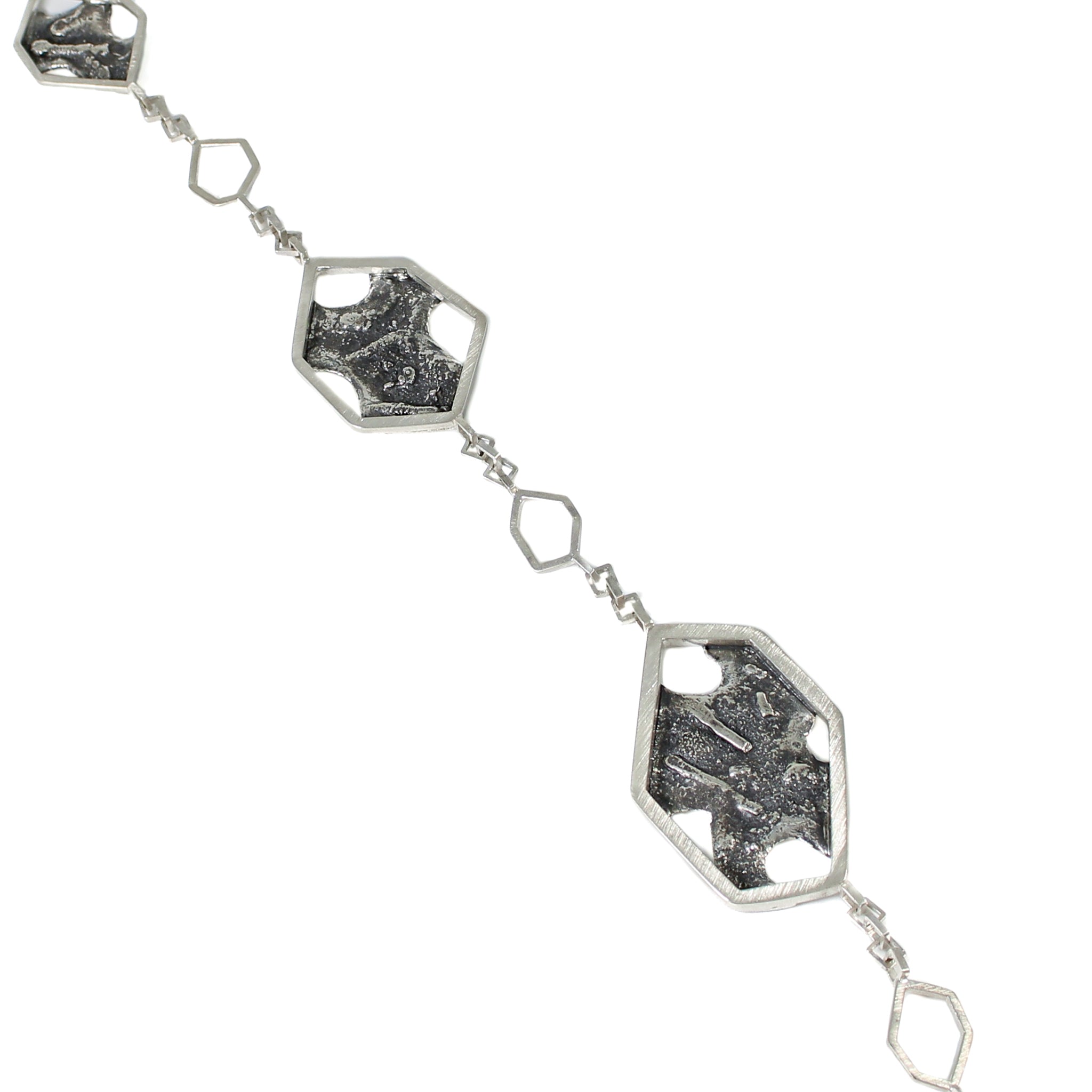 3 asymmetric hexagons in descending size, framing blackened and roughly textured blackplates, each with melted holes in it. Each hexagon is separated by an inch of square link chain with a smaller, hexagonal link in the middle.