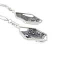 Load image into Gallery viewer, Close-up side view of blackened, brutalist inspired texture on backplate of earrings. Silver mesh, blobs and grit can be seen in the texture. The backplate is framed by an asymmetric hexagon, attached to some square links. The other earring is seen blurred in the background. 
