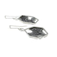 Load image into Gallery viewer, Close-up side view of blackened, brutalist inspired texture on backplate of earrings. Silver mesh, blobs and grit can be seen in the texture. The backplate is framed by an asymmetric hexagon, attached to some square links and a custom made square ear wire. The other earring is seen blurred in the background. 
