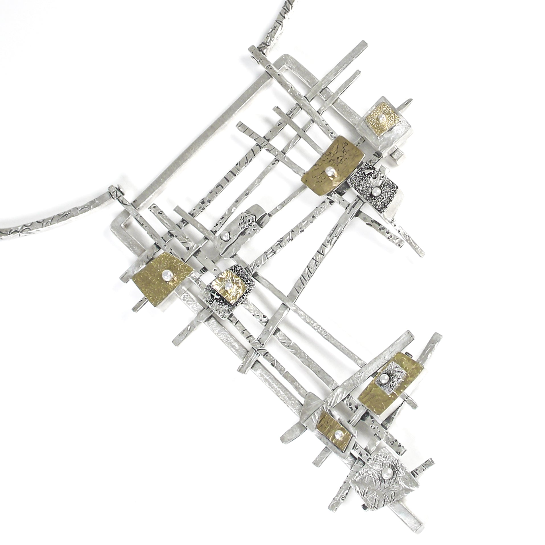 A substantial modernist inspired sterling silver necklace, with 18 karat gold and fine silver embellishments. The main pendant has multiple heavily textured silver bars intersecting in a random pattern, forming an grid structure of a loosely defined right-angle triangle. On top the grid are nine asymmetric rectangular shapes, arranged in three groups, across three sections of the grid. Each is a different size and height, and made with differing techniques