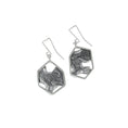 Load image into Gallery viewer, Sterling silver modern dangle earrings, on white background. Each earring has a large asymmetric hexagon, framing a blackened and brutalist textured backplate. This is attached to some square chain links finished with a custom made square shaped ear wire.
