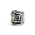 Load image into Gallery viewer, Sterling silver overlapping wrap ring, with melted edges and an oxidized rustic surface texture. A square, translucent, blue moonstone is roughly bezel set in the center of the ring. 
