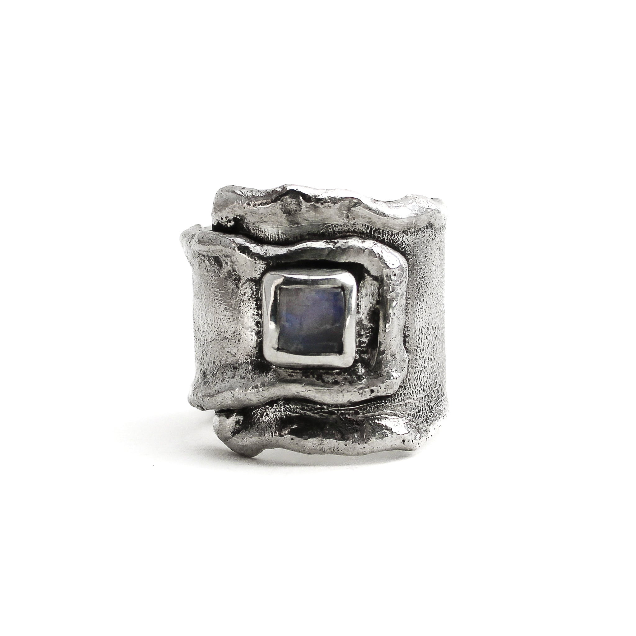 Sterling silver overlapping wrap ring, with melted edges and an oxidized rustic surface texture. A square, translucent, blue moonstone is roughly bezel set in the center of the ring. 