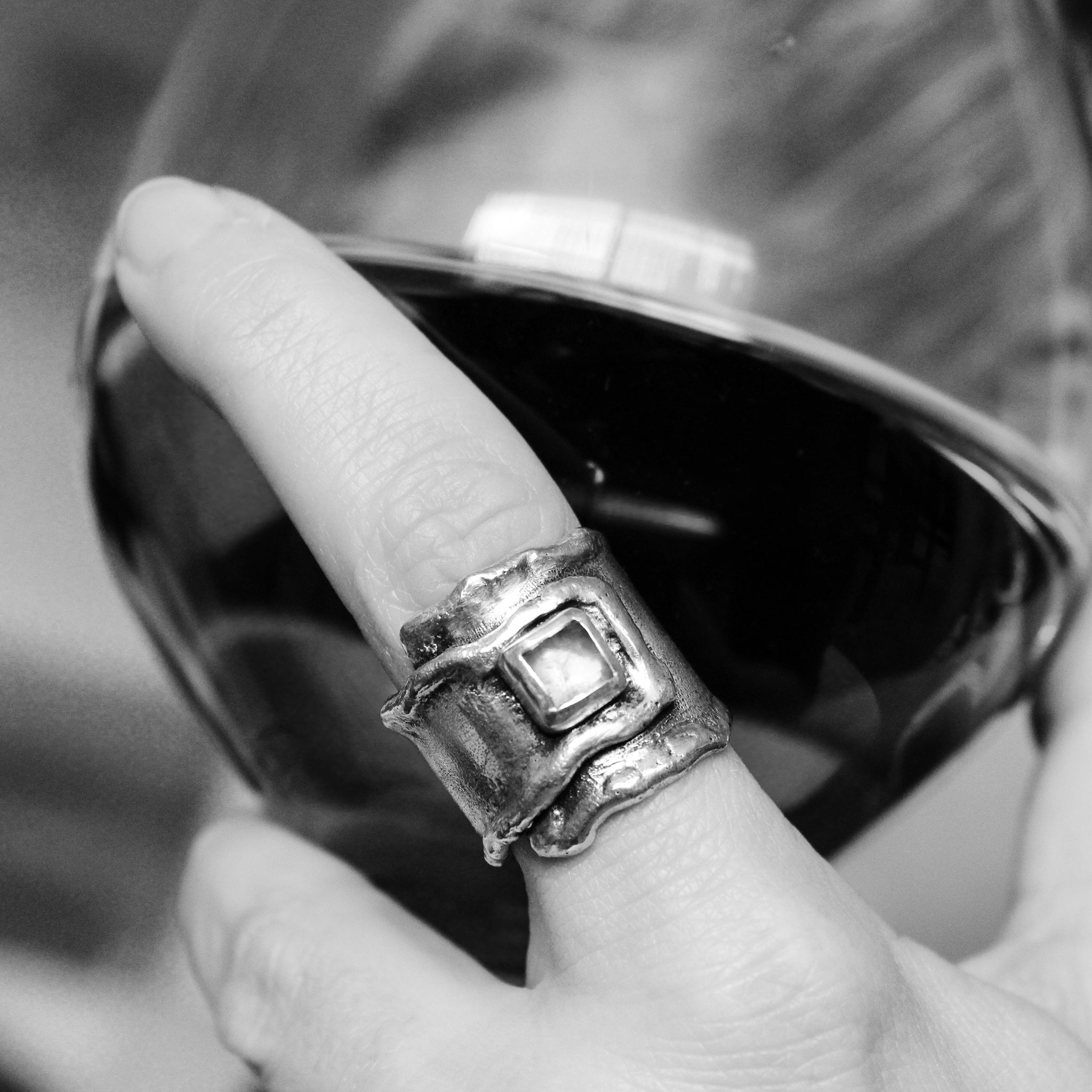 Black and white close-up of hand, holding a glass of red wine. Focus in the on the sterling silver wrap ring, with square moonstone on pointer finger.