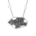 Load image into Gallery viewer, A close up, front view of a modern sterling silver pendant, featuring a large, asymmetric hexagon frame over a blackened, fused and brutalist textured blackplate. There are 4 melted holes in the backplate. The pendant is hung from a square link in link chain, with a small open hexagon 1.5" up the chain on either side.
