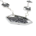 Load image into Gallery viewer, A necklace, laying flat. It is a close-up view of the side of the pendant, showing the edge of a hexagonal frame, highlighting the scratched texture on it. There are 3 other smaller hexagons on a square link chain, blurred in the background.  
