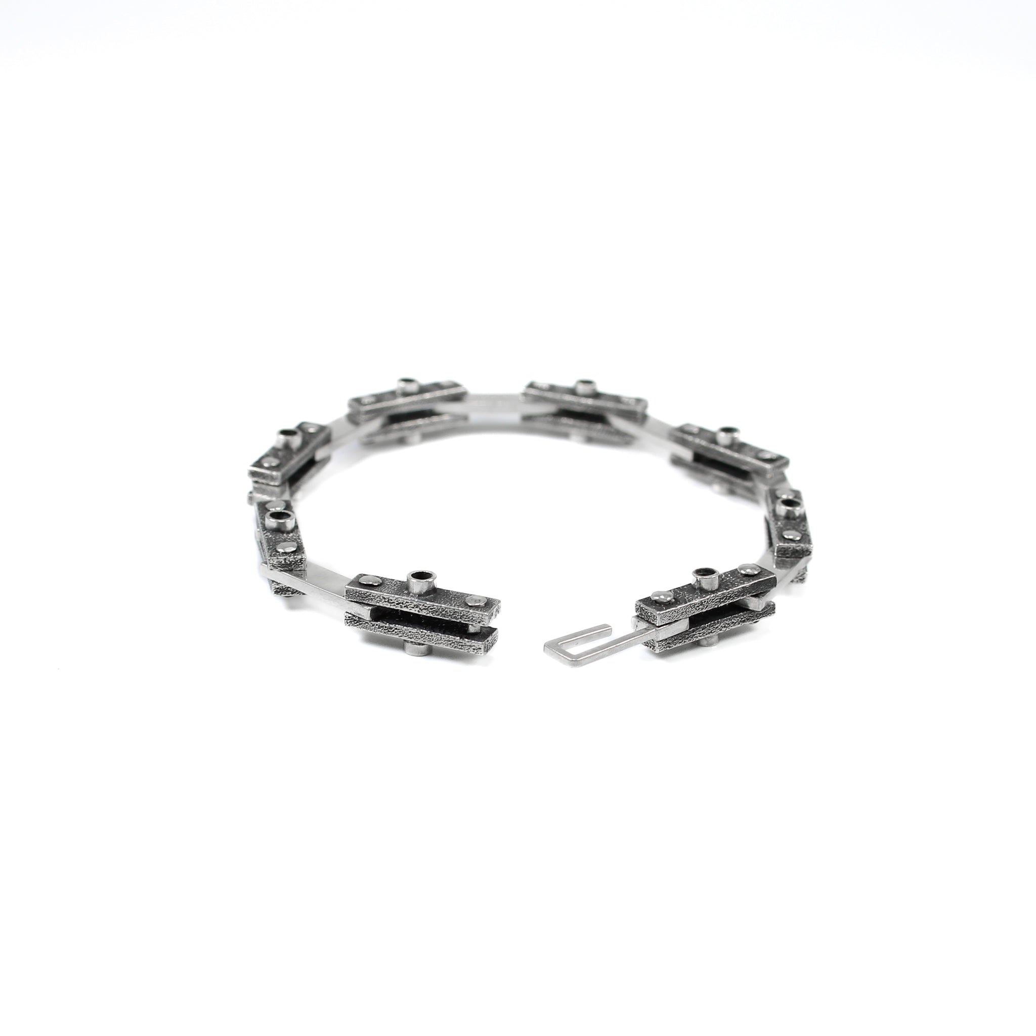 Unique industrial sterling silver bicycle-style chain bracelet. Every other link features a textured black finish with a 3mm tube soldered in the center on both sides and the alternate link is smooth and polished. Each link is connected by roughly finished rivets. Side view, bracelet is undone and the hook clasp is visible.  