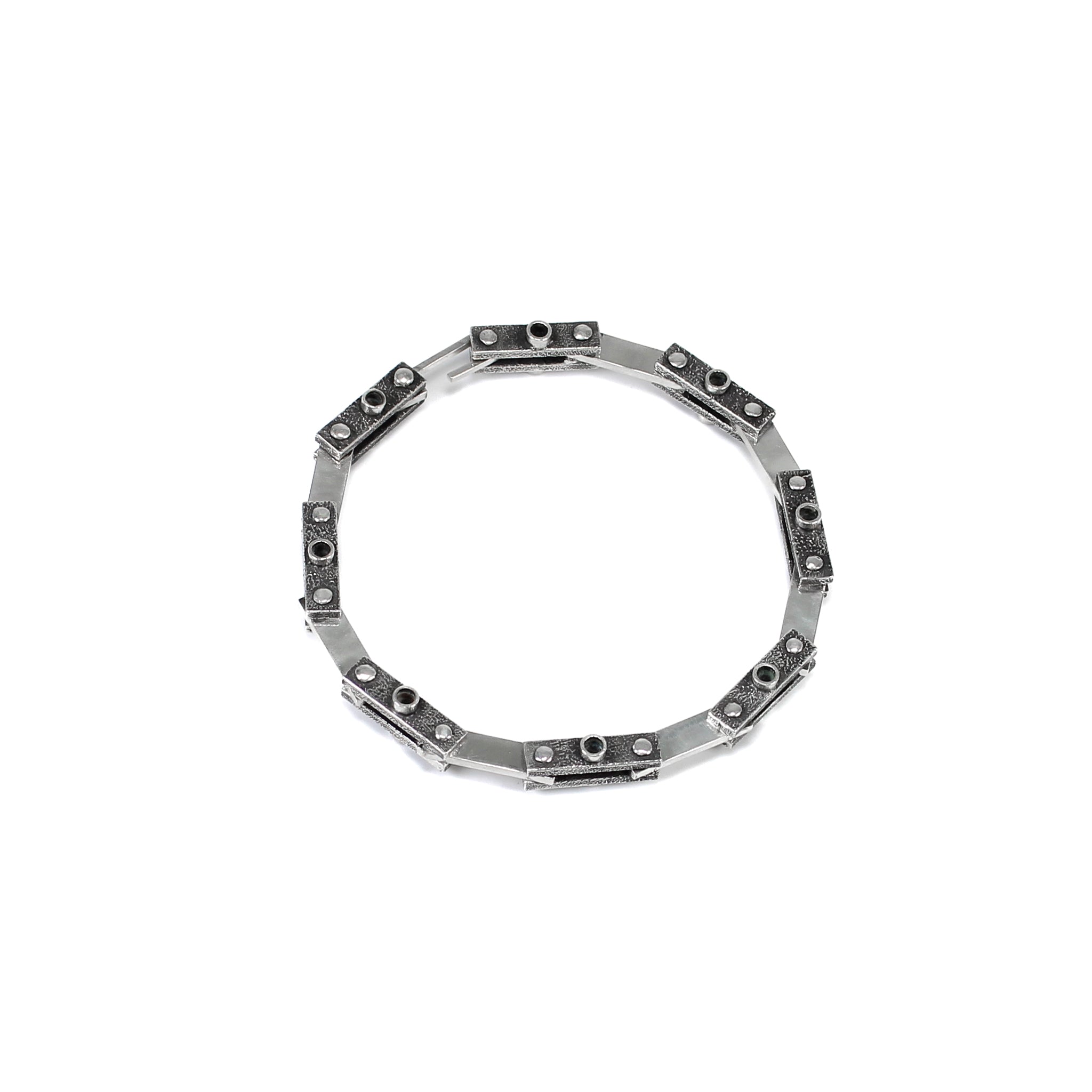 Unique industrial sterling silver bicycle-style chain bracelet. Every other link features a textured black finish with a 3mm tube soldered in the center on both sides and the alternate link is smooth and polished. Each link is connected by roughly finished rivets. Top view of braceletm it is closed and positioned in a circle on a white background. 