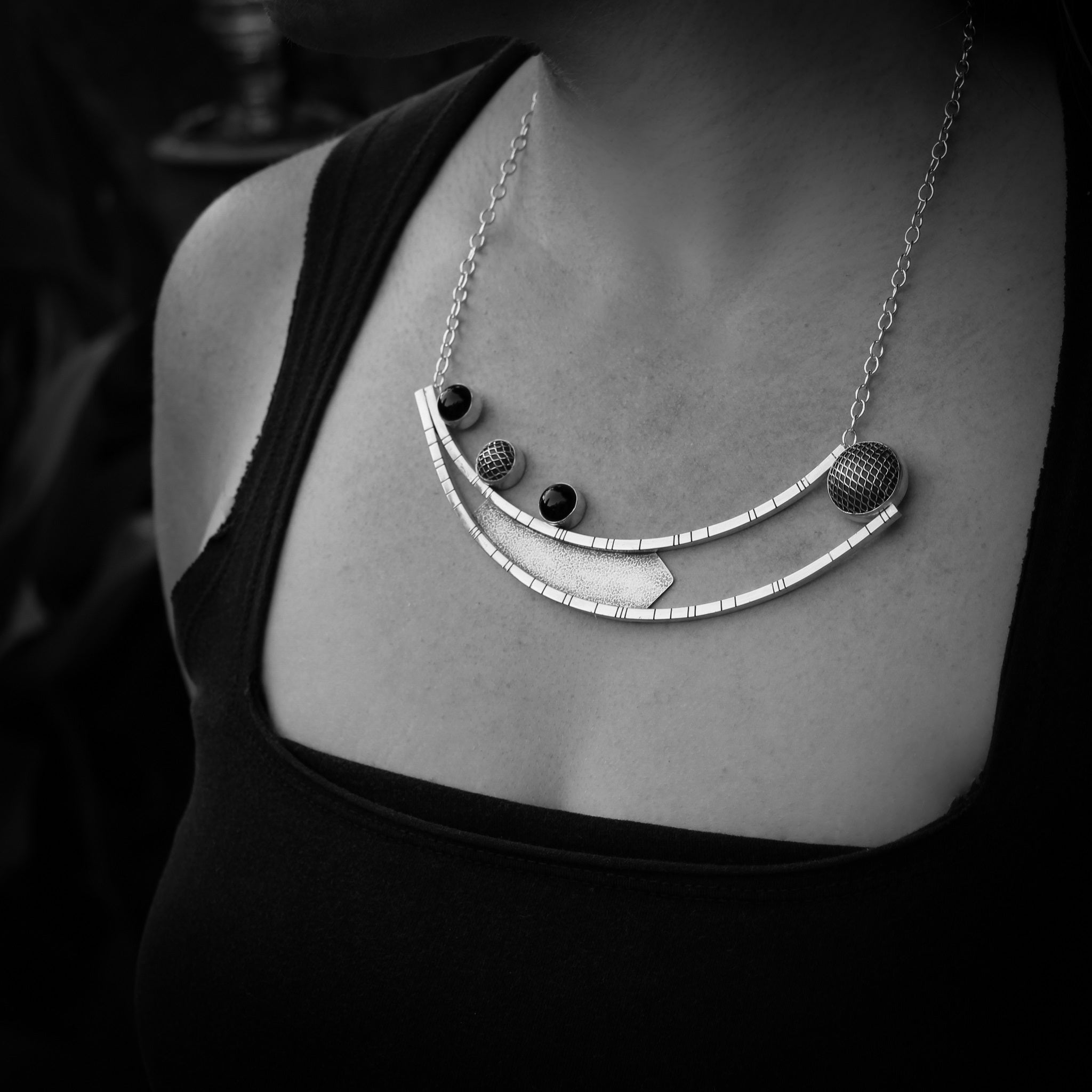 Black and white close up of woman's neckline.  She is wearing a black shirt and a handmade modern geometric silver pendant. 