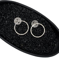 Load image into Gallery viewer, Unique handmade earrings with a blackened, round, brutalist-textured disc. A ring runs through the center, and a larger hoop hangs through the ring, mimicking a door knocker. Random black lines accentuate the face of the hoop for added character. Earrings are in a black dish, with black pebbles, on a white background.
