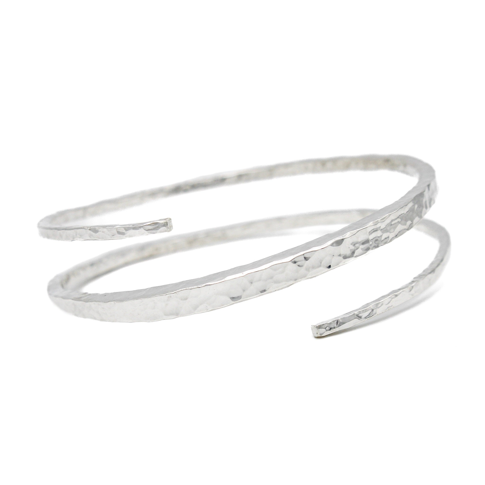 Sterling silver bracelet with a hammered texture. The bangles ends bypass eachother and create a single coil.  It is thicker in the middle and tapers towards either end. Bracelet is on a white background and facing forward