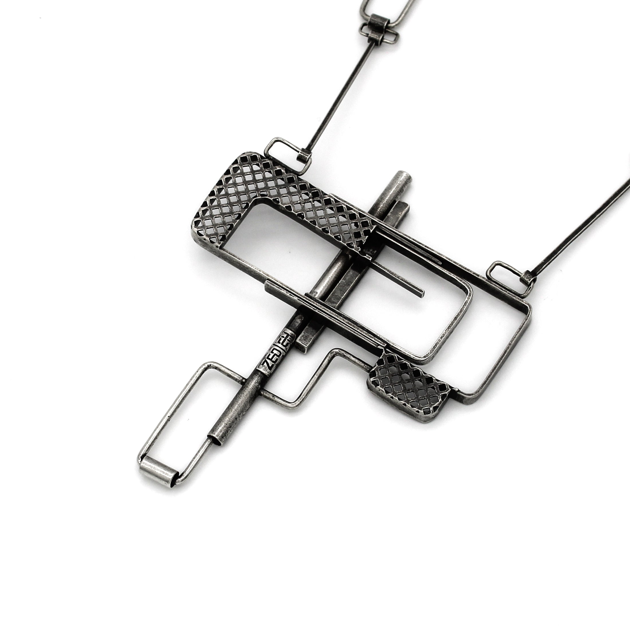 Back of of sterling silver industrial-style pendant featuring a geometric design with a combination of open rectangular frames and mesh-textured sections. A central horizontal bar intersects the piece, creating a layered, puzzle-like effect. The pendant has an oxidized, matte finish and is suspended from a chain with angular links that complement the design's structural feel. Zed Eh Design's logo can be seen on the long bar. 