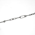 Load image into Gallery viewer, The image shows a close-up of a silver chain with various rectangular and geometric-shaped links. The chain has an industrial and minimalist design, with some links being elongated rectangles, while others are smaller and more compact. The background is white, providing a clean and clear view of the chain's structure and details.
