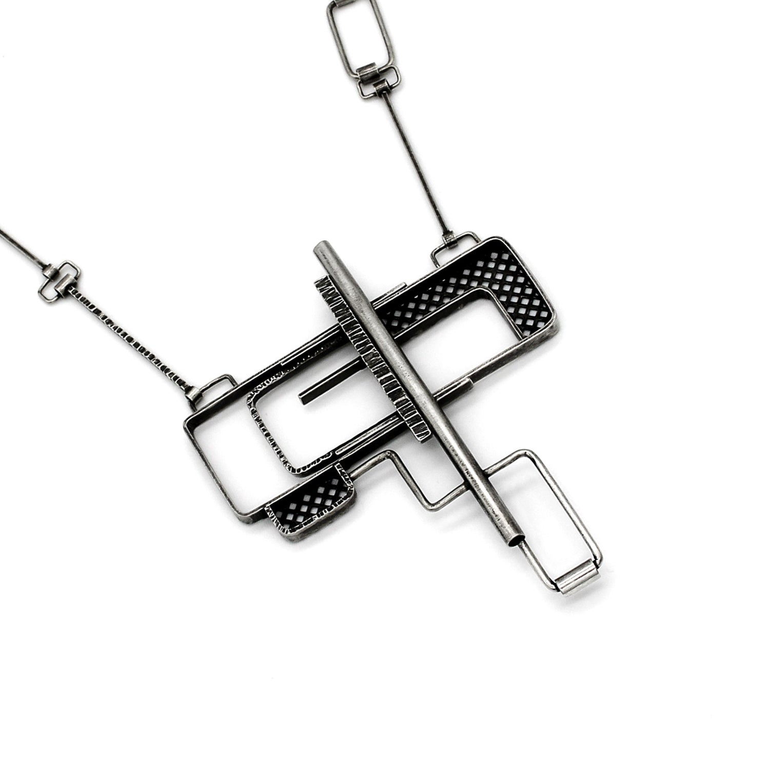 Front view of sterling silver industrial pendant featuring a geometric design with a combination of open rectangular frames and mesh-textured sections. A central horizontal bar intersects the piece, creating a layered, puzzle-like effect. The pendant has an oxidized, matte finish and is suspended from a chain with angular links that complement the design's structural feel.