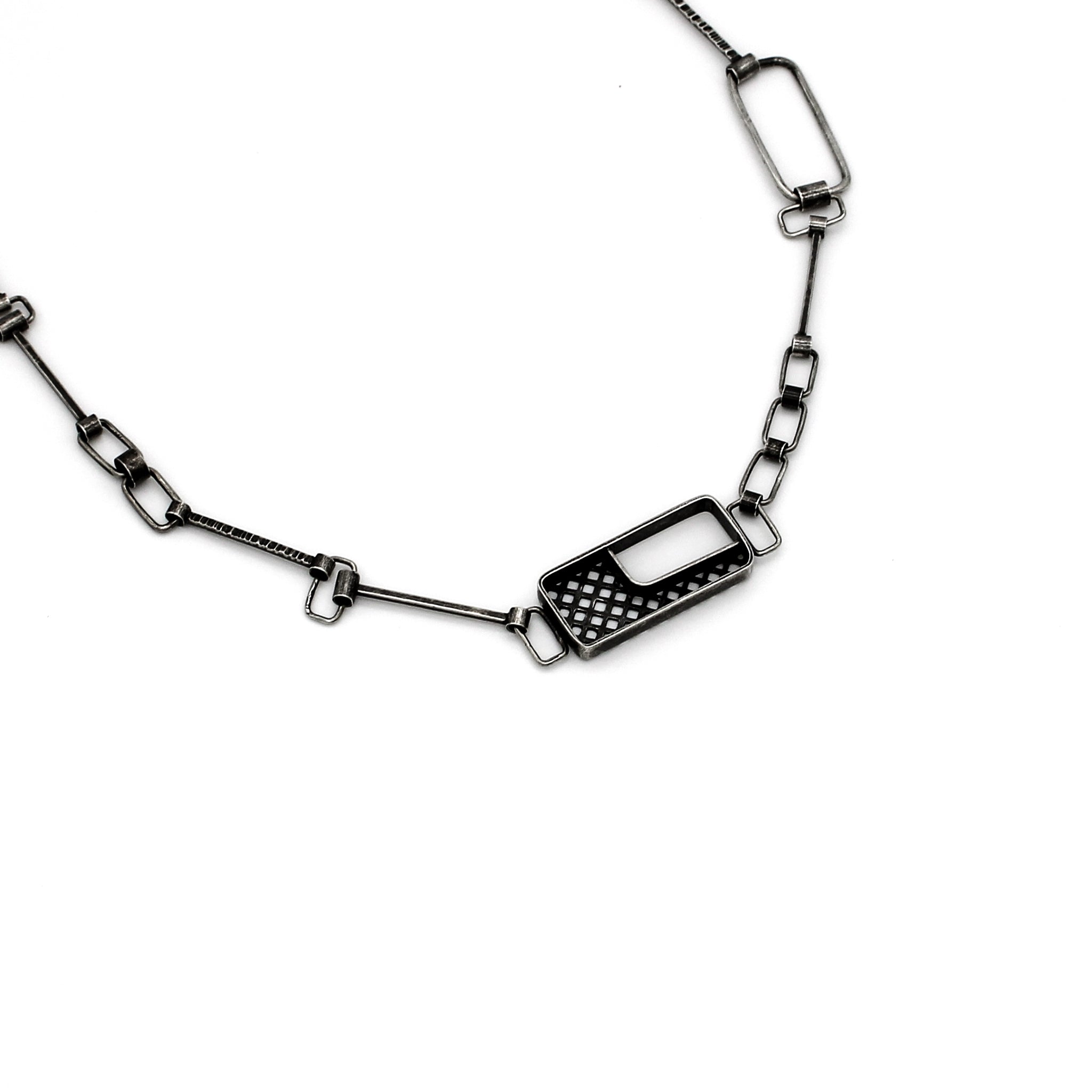 Sterling silver necklace with a unique puzzle clasp design featuring a geometric, rectangular charm with an open section and a grid-like pattern. The necklace consists of an assortment of interconnected rectangular and square chain links, giving it an intricate and modern look.