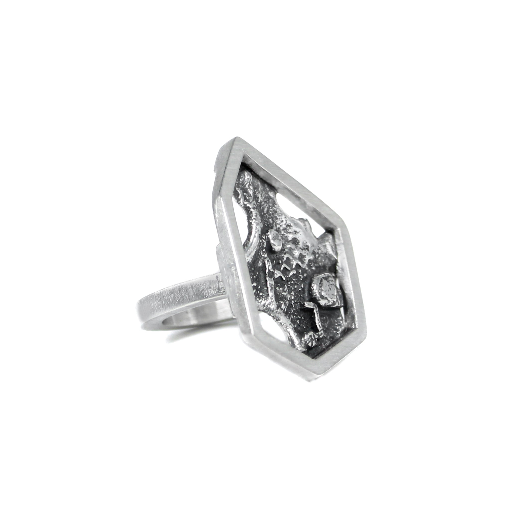 45 degree angled side view of unique contemporary sterling silver ring featuring a single, asymmetric hexagon framing a blackened, melted, and fused texture backplate. 