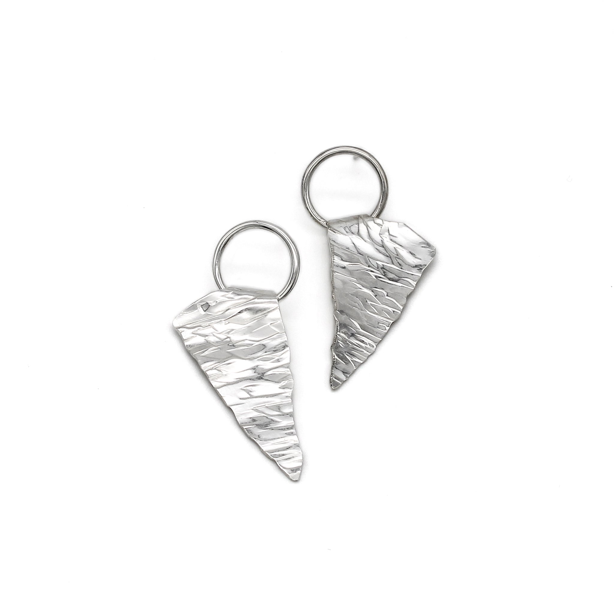 A unique pair of handmade silver earrings, each a rough triangular shape with a textured surface resembling ice. They are suspended from a sterling ring attached to ear posts.