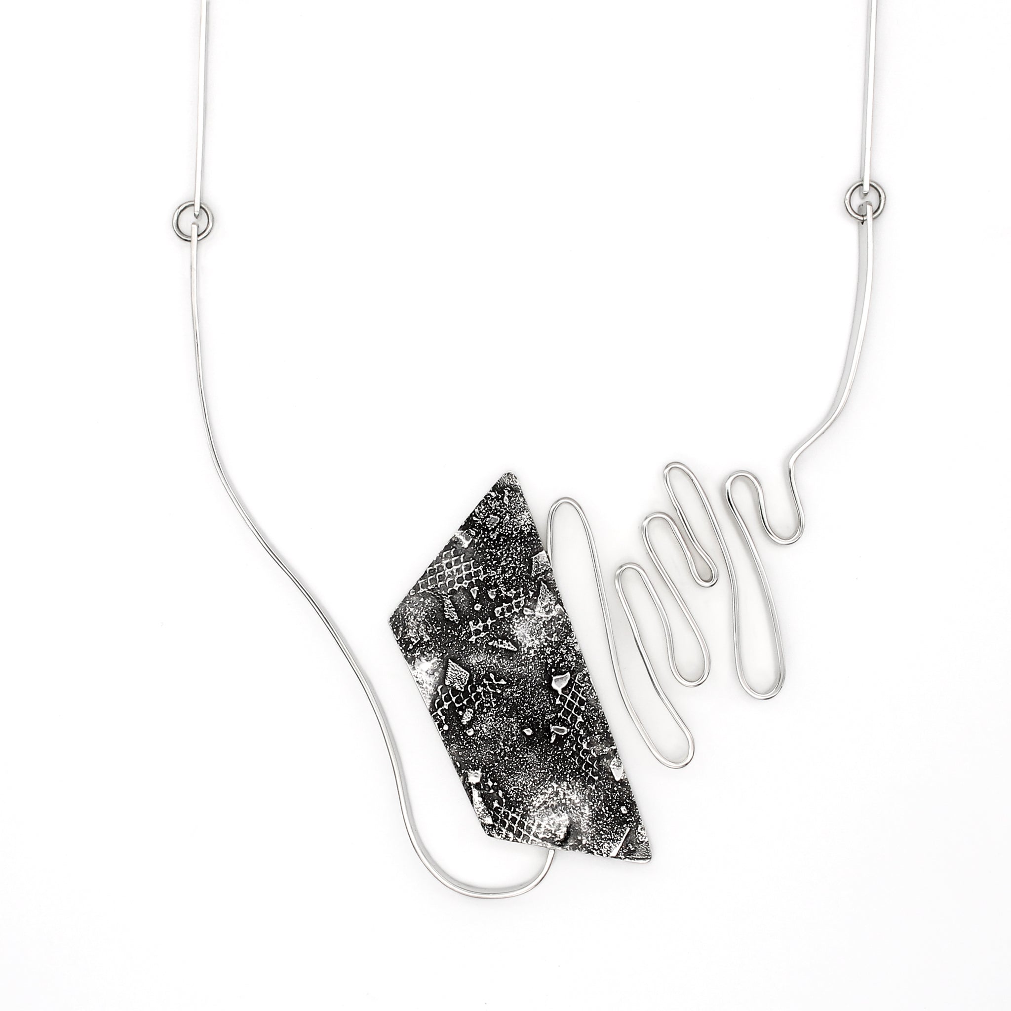 A modernist inspired handmade sterling silver necklace showcasing an undulating bar on the left side, mimicking soundwaves, culminating at the left side of an asymmetric pentagon hollowform. The hollowform has a blackened, heavily textured surface, evoking a brutalist sensibility. Emerging from the bottom of the hollowform, the silver bar creates the illusion of continuity as it curves upward, connecting to a bar and link chain.