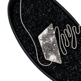 Load image into Gallery viewer, A modernist inspired handmade sterling silver necklace showcasing an undulating bar on the left side, mimicking soundwaves, culminating at the left side of an asymmetric pentagon hollowform. The hollowform has a blackened, heavily textured surface, evoking a brutalist sensibility. Emerging from the bottom of the hollowform, the silver bar creates the illusion of continuity as it curves upward, connecting to a bar and link chain. Pendant is in a black dish with black pebbles. 
