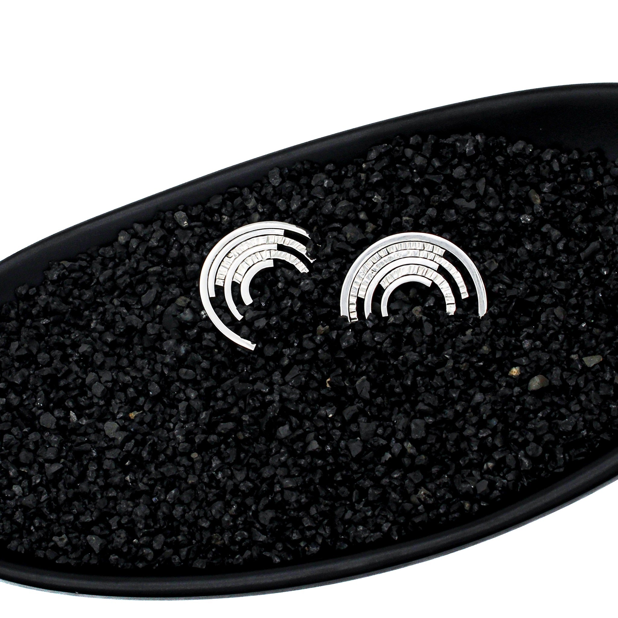 Front view of modern sterling silver ear studs, each with 6 partial concentric circles in a black dish with black pebbles.