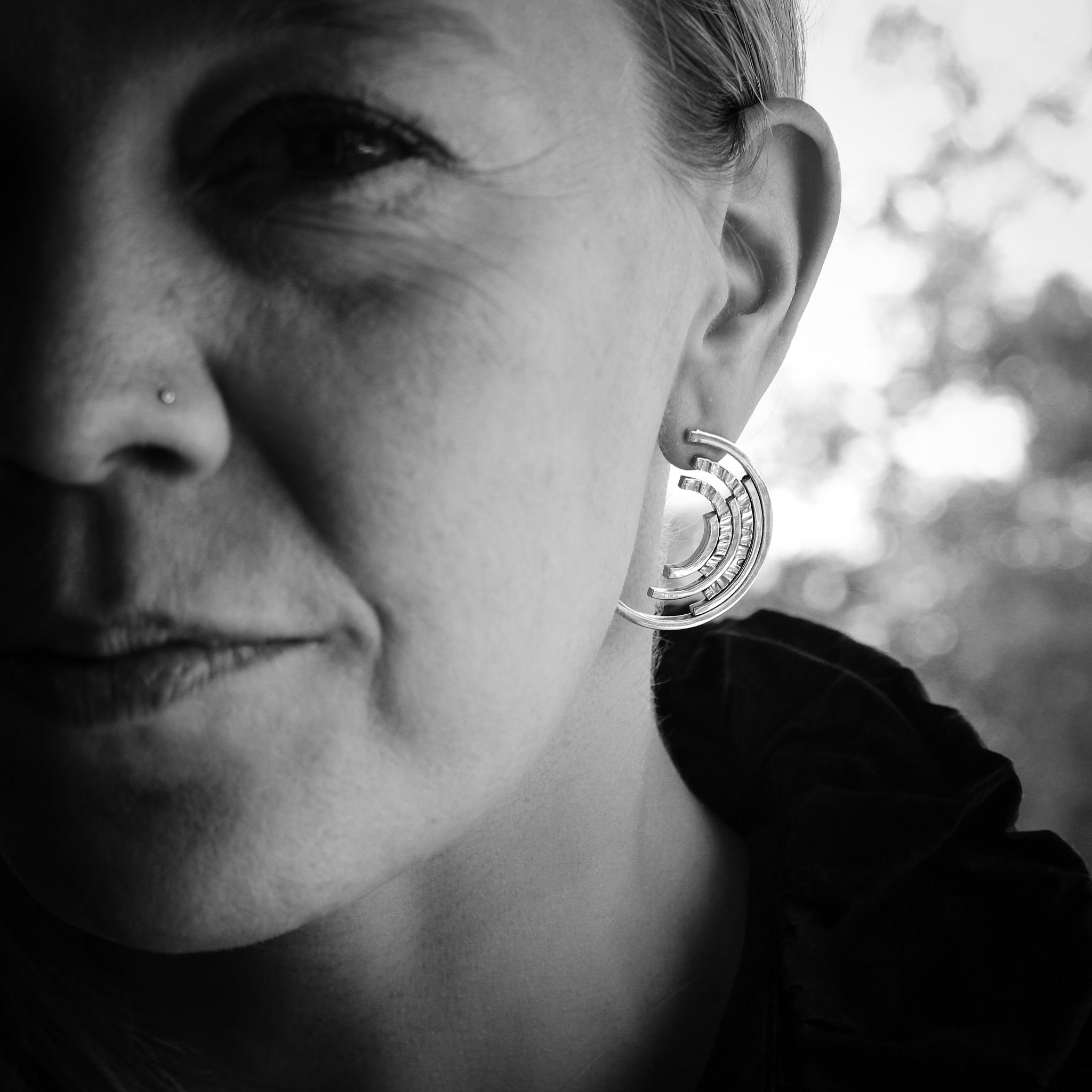 Close up black and white photo of woman's left side of face, wearing sterling silver ear stud with 6 concentric circles