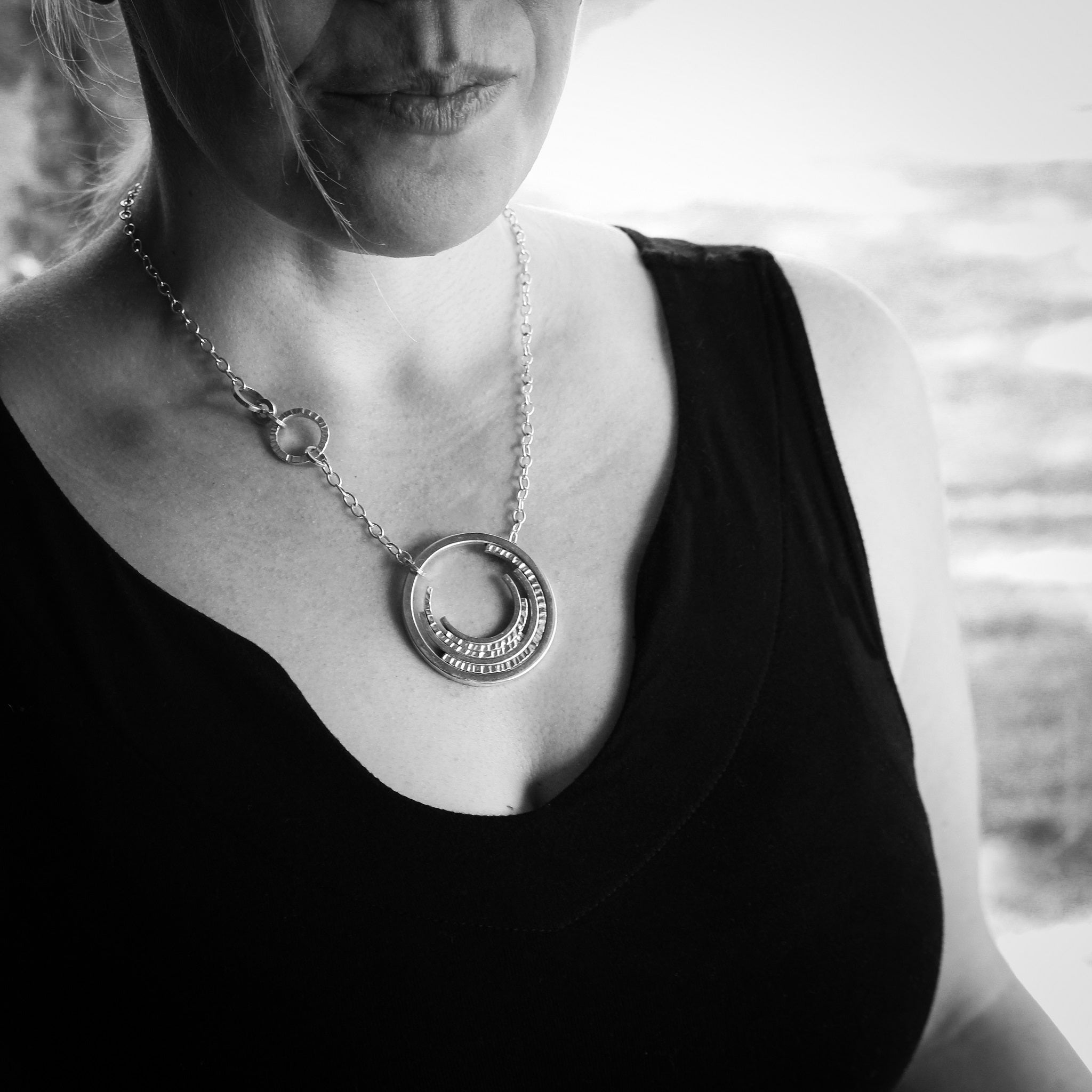 Black and White photo of woman’s decolletage in black shirt wearing contemporary silver inner concentric circle necklace 