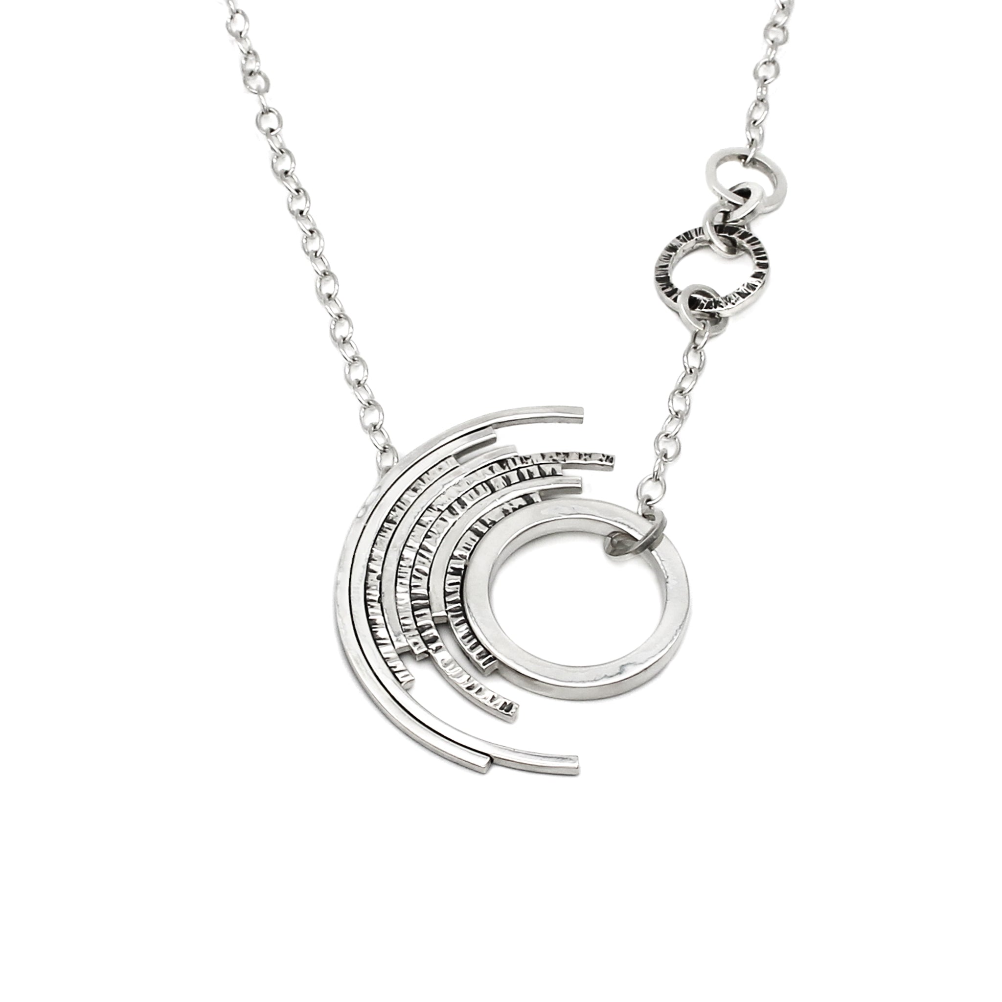 A handmade sterling silver asymmetrical pendant with a single thick circle surrounded by 7 outer concentric partial circles, some with featuring a chisel texture