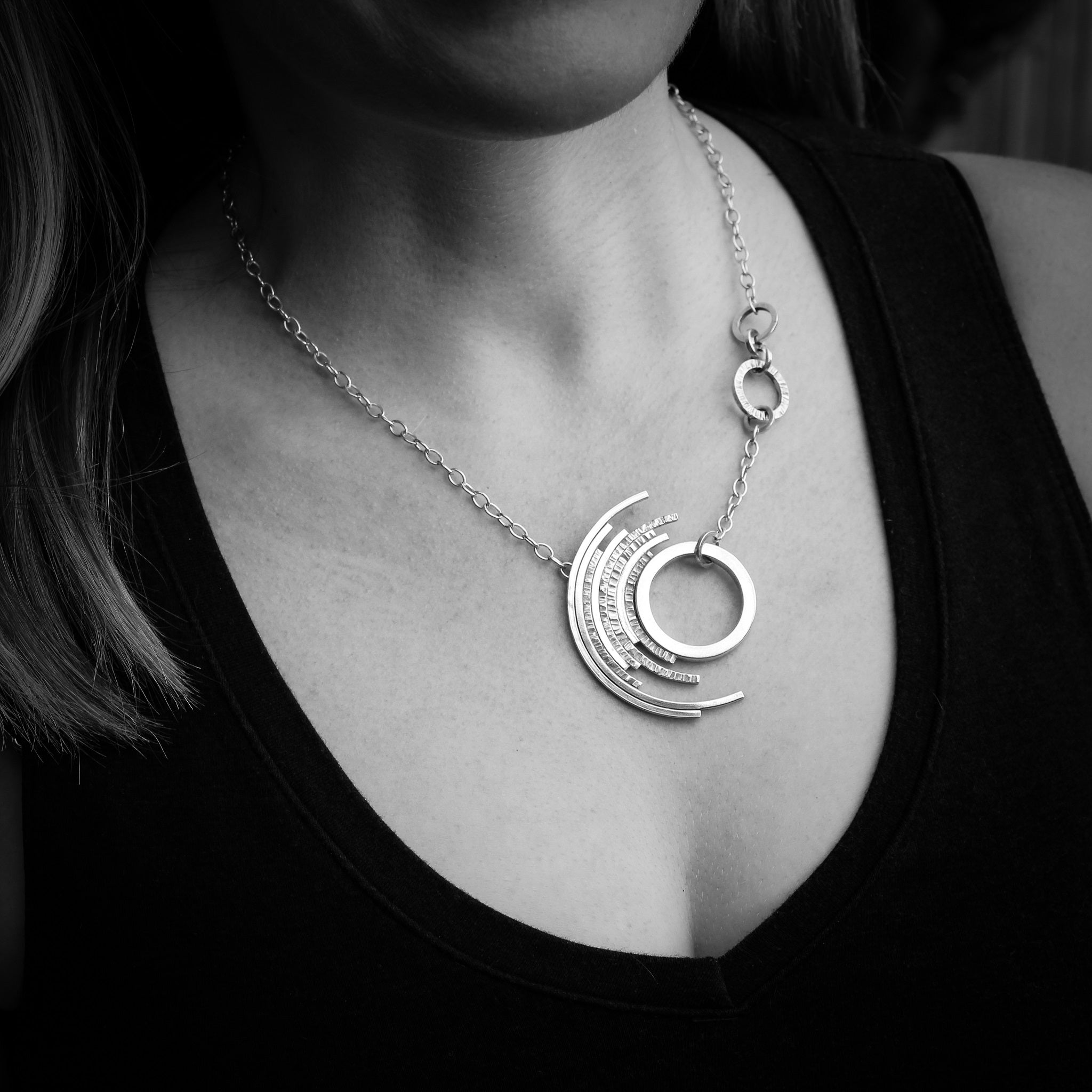 Black and White photo of woman’s decolletage in black shirt wearing contemporary silver outer concentric circle necklace 